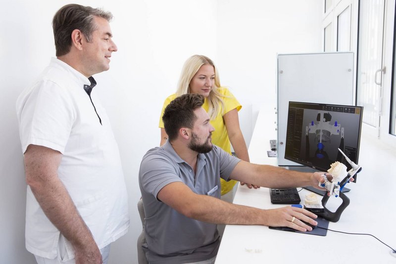 Team aus Zahnarzt, ZFA und Zahntechniker besprechen einen Fall am PC