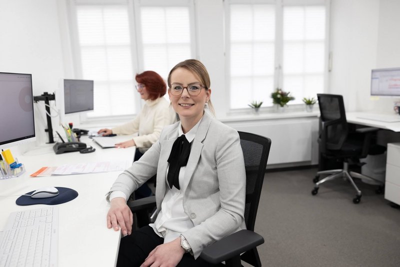 ZMV sitzt an ihrem Schreibtisch und schaut lächelnd in die Kamera 